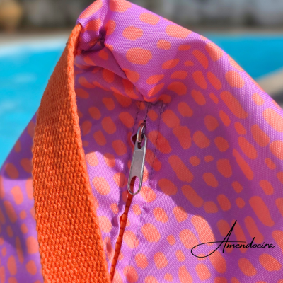 Bolsa rosa e laranja com fecho metálico junto a piscina