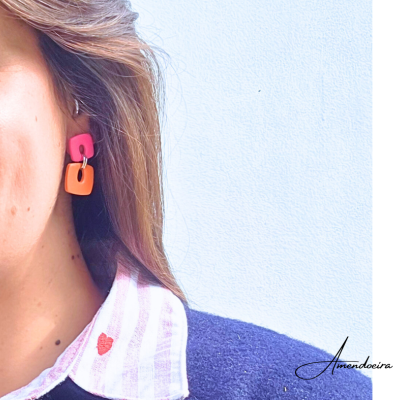 Brincos coloridos rosa e laranja usados por mulher com camisa e suéter.