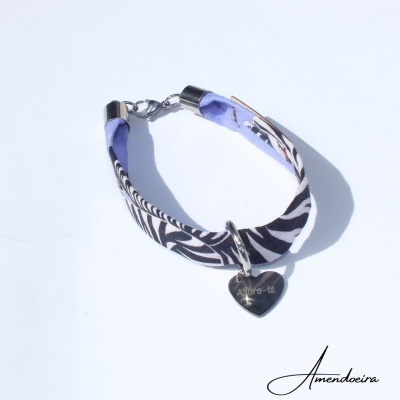 Pulseira de tecido com padrão preto, branco e roxo e pendente em forma de coração com texto