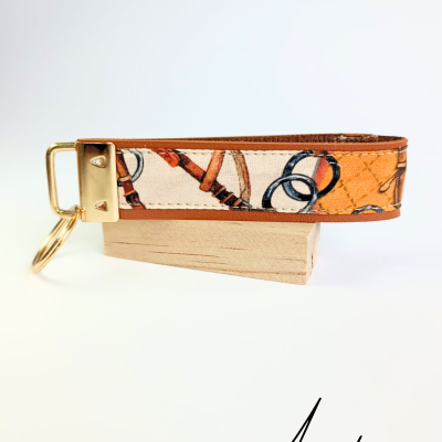 Chaveiro estampado em tecido com detalhes em couro castanho e fecho dourado sobre base de madeira