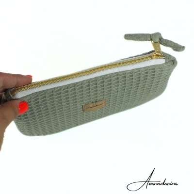 Estojo verde com textura quadrada, fecho dourado e etiqueta castanha