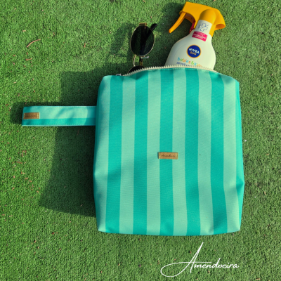 Bolsa azul turquesa riscada com óculos de sol e frasco Nivea Baby Sun numa superfície verde