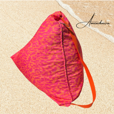 Almofada triangular rosa e laranja com alça laranja na areia junto ao mar