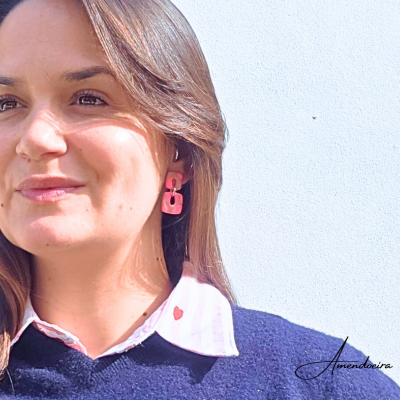 Brincos femininos rosa retângulo usados por mulher com camisa branca riscada e suéter azul.