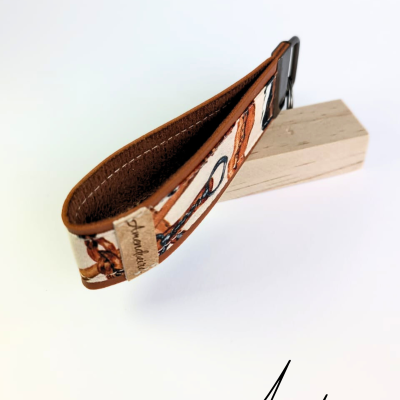 Pulseira em tecido e couro com etiqueta Amendoeira apoiada em bloco de madeira