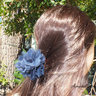 Mola de cabelo azul escura em cabelo castanho com folhagem ao fundo