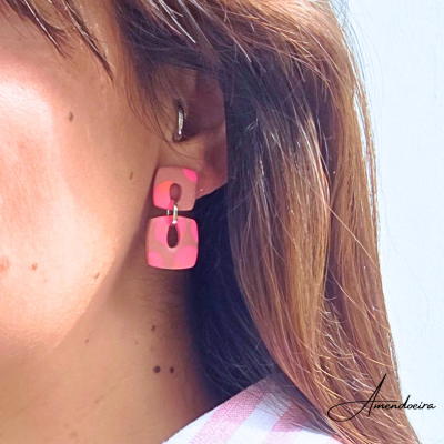 Brincos de resina rosa com padrão de manchas, formato quadrado, usados numa orelha