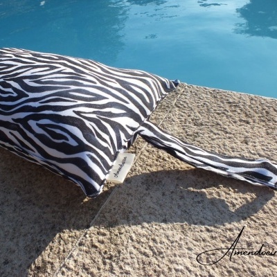 Almofada padrão zebra com alça sobre pedra ao lado de uma piscina