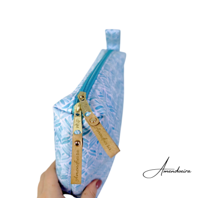 Necessaire azul claro com padrão de folhas e fecho de correr com puxadores em couro