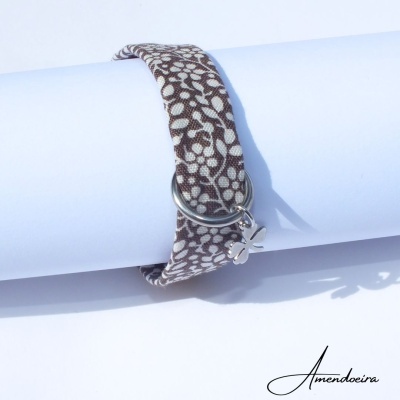 Pulseira em tecido castanho com folhas brancas e pendente de trevo prateado