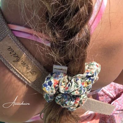 Menina com rabo de cavalo preso por elástico floral e faixa cinza com etiqueta ao ar livre