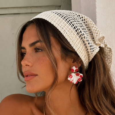 Mulher com lenço branco tipo rede na cabeça e brincos florais vermelhos e brancos