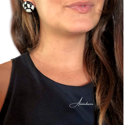 Brincos redondos pretos e brancos com padrão marmoreado usados por mulher com blusa preta