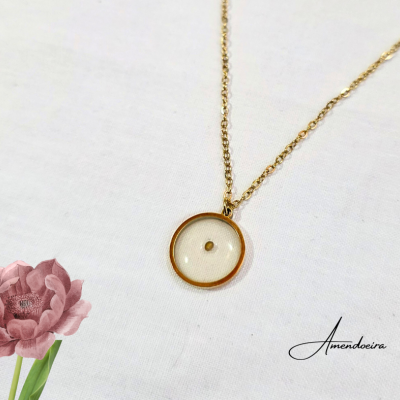 Colar dourado com pendente redondo de vidro com ponto dourado, sobre fundo branco com flor rosa e texto Amendoeira