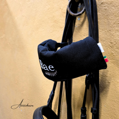 Protetor de rédea preto com texto 'Rae' pendurado numa parede bege