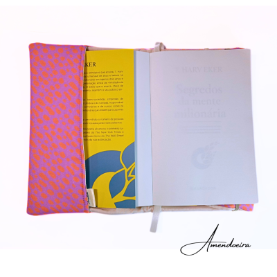 Livro aberto numa capa rosa com pintas laranjas, texto visível na página do livro