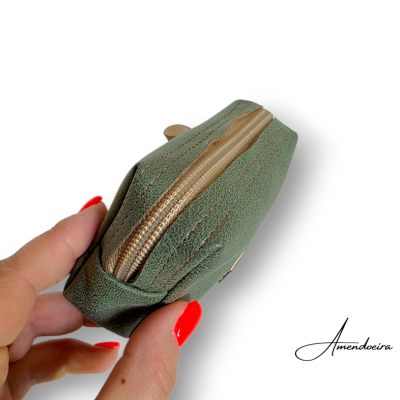 Necessaire pequena verde com fecho dourado segurada por mão com unhas vermelhas