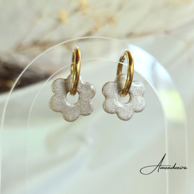 brincos dourados com pendente flor prateada brilhante em suporte transparente