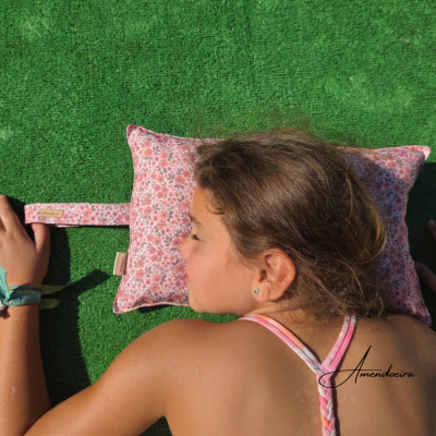 Almofada floral rosa com alça ao lado e pessoa deitada ao lado sobre relva verde