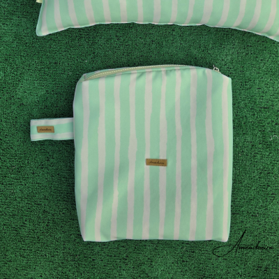 Bolsa listrada verde água e branca com fecho zíper sobre superfície verde