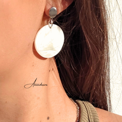 Brinco pendente prateado e creme numa orelha com cabelo castanho