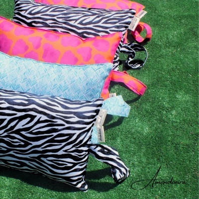 Três almofadas coloridas e estampadas sobre relva artificial com assinatura Arandaira