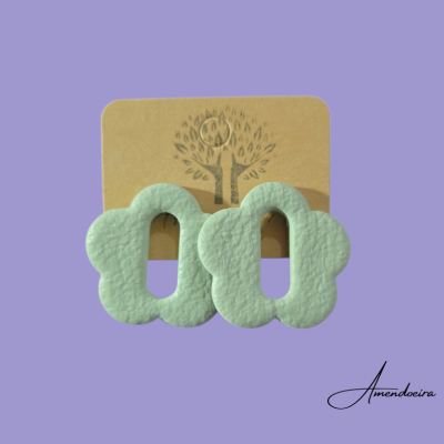 Brincos flor verde claro texturado sobre cartão castanho com árvore