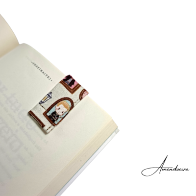 Marcador de livro tecido com padrão de janelas e personagens numa página de livro