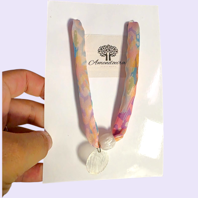 Colar com fita de tecido colorida e pendente branco, em cartão com logotipo Amendoeira