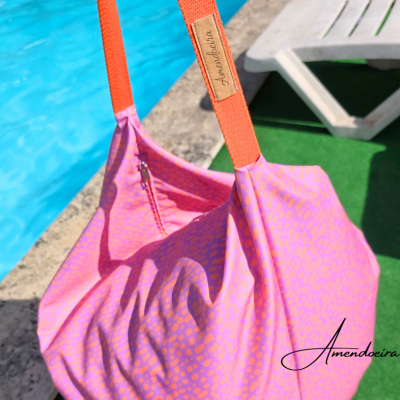 Mala rosa com padrão laranja e alças laranja junto a piscina