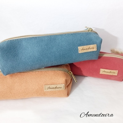 Três bolsas de maquilhagem retangulares em azul, cor-de-rosa e bege com etiquetas Amendoeira