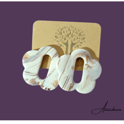 Brincos marmorizados em resina branca e castanha, com formato irregular, em cartão castanho e fundo roxo.