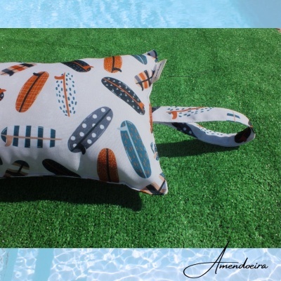 Almofada retangular com padrão de pranchas de surf coloridas junto a piscina e relva artificial