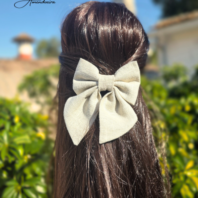 Laço bege de tecido em cabelo castanho escuro com fundo de plantas e edifícios.