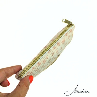 Estojo fino branco com padrão listrado e fecho dourado, mão segurando