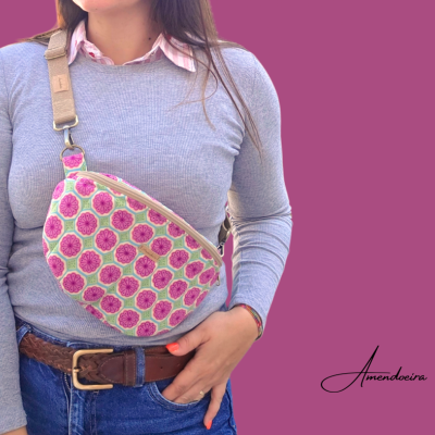 Bolsa tipo pochete com padrão floral rosa e verde, alça bege, usada por mulher com camisa cinza e jeans