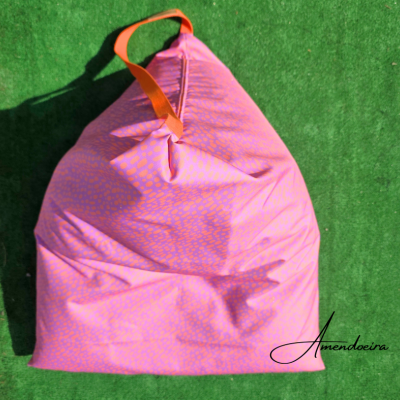 Saco almofada de pufe rosa com padrão laranja e alça alaranjada sobre relva artificial verde
