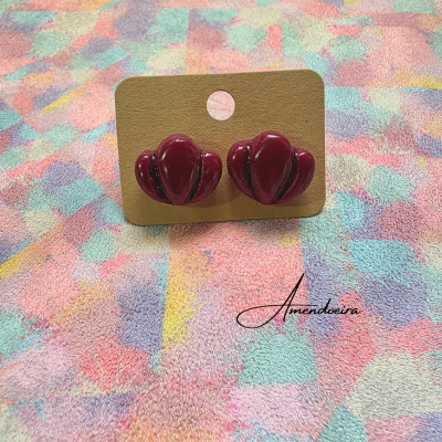 Brincos castanhos escuros em formato de coração sobre cartão castanho com fundo colorido.