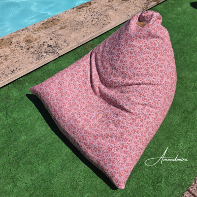 Pufe floral rosa sobre relva sintética ao lado de piscina