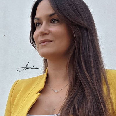 Mulher de cabelo castanho com blazer amarelo e colar de pérola