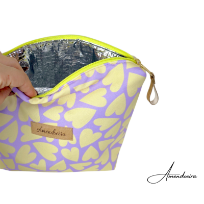 Necessaire com padrão de corações amarelos em fundo lilás com interior térmico prateado e zíper amarelo.