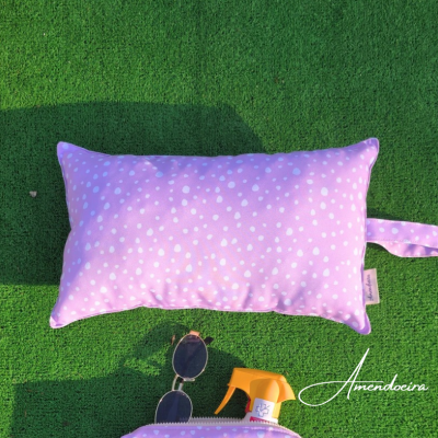 Almofada rosa com bolinhas brancas sobre relva artificial verde com óculos de sol e garrafa amarela