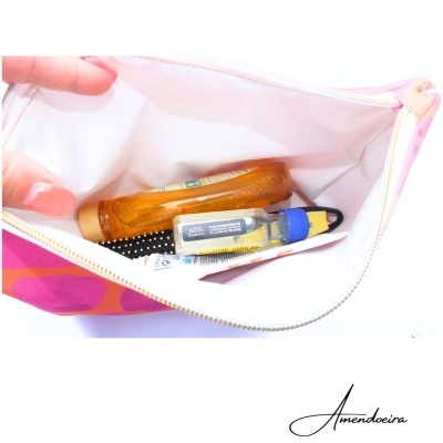 Bolsa rosa aberta com frasco laranja, frasco pequeno azul e amarelo, escova preta e tubo branco