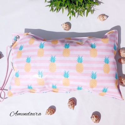 Travesseiro com padrão de abacaxis amarelos em fundo de listras rosas e brancas, com cordão e conchas ao redor