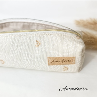 Estojo bege com padrão branco e detalhes cor de mostarda com fecho dourado e etiqueta Amendoeira