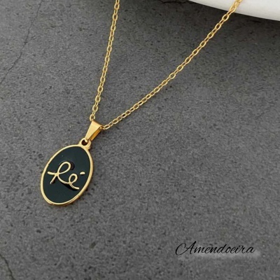Colar dourado com pendente oval preto e dourado sobre fundo cinza