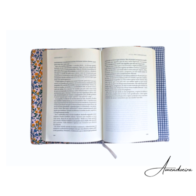 Livro aberto sobre suporte almofadado com tecidos estampados e assinatura Amendoeira