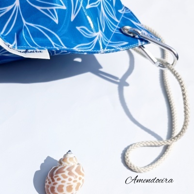 Saco azul com padrão branco, mosquetão com corda e concha em fundo branco