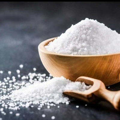 Tigela de madeira com sal grosso branco e pá de madeira com sal ao lado sobre fundo escuro