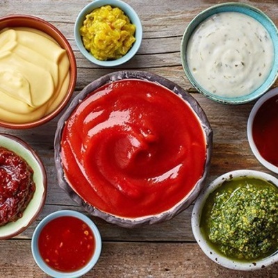 Sete tigelas com molhos coloridos sobre mesa de madeira